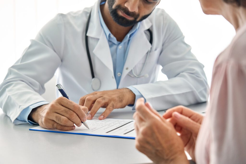 Indian male doctor consulting senior old patient filling medical form.